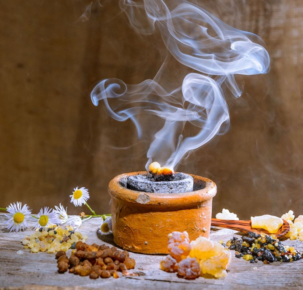 Aromatic dhoop incense burning in a clay pot surrounded by flowers and natural resins